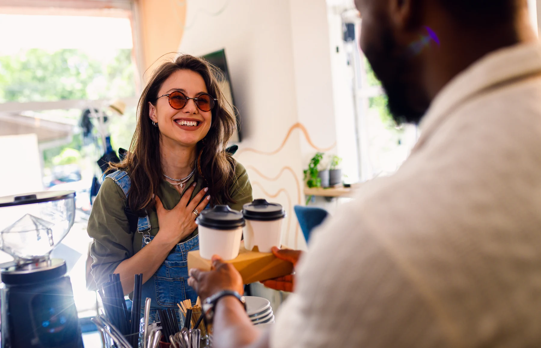 A smiling customer receiving takeaway coffees from a barista at a café
