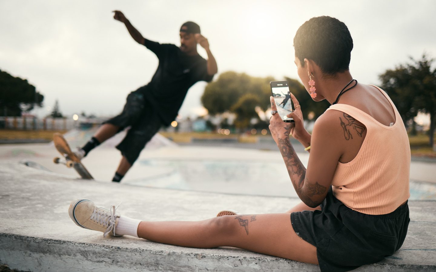 A woman filming a friend’s skateboard trick on her phone at a skate park
