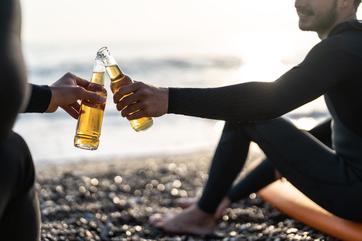 Two surfers clink beer bottles on the beach