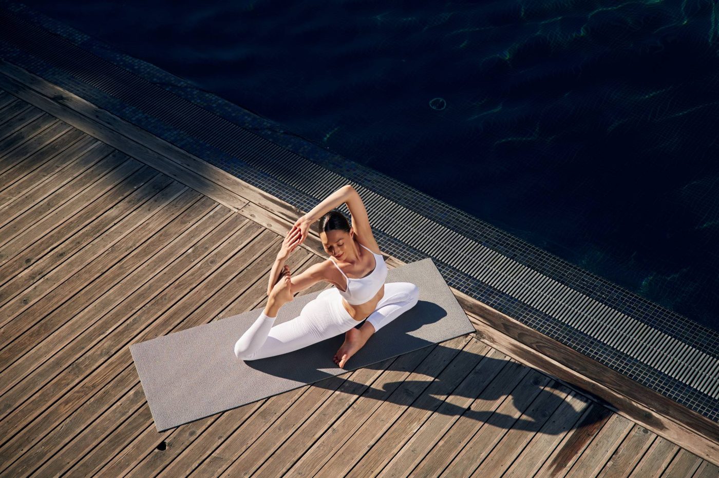A woman holding a yoga pose on a mat by the pool