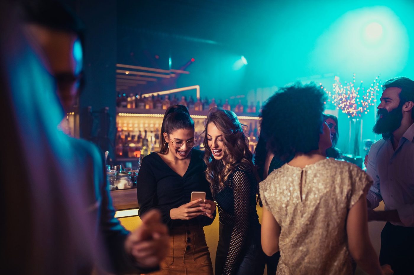 Friends look at a phone together in a busy bar