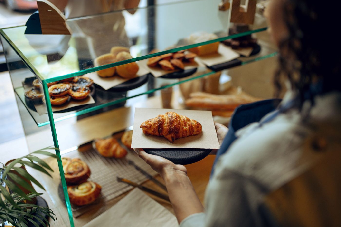 A customer is handed a croissant from a bakery display
