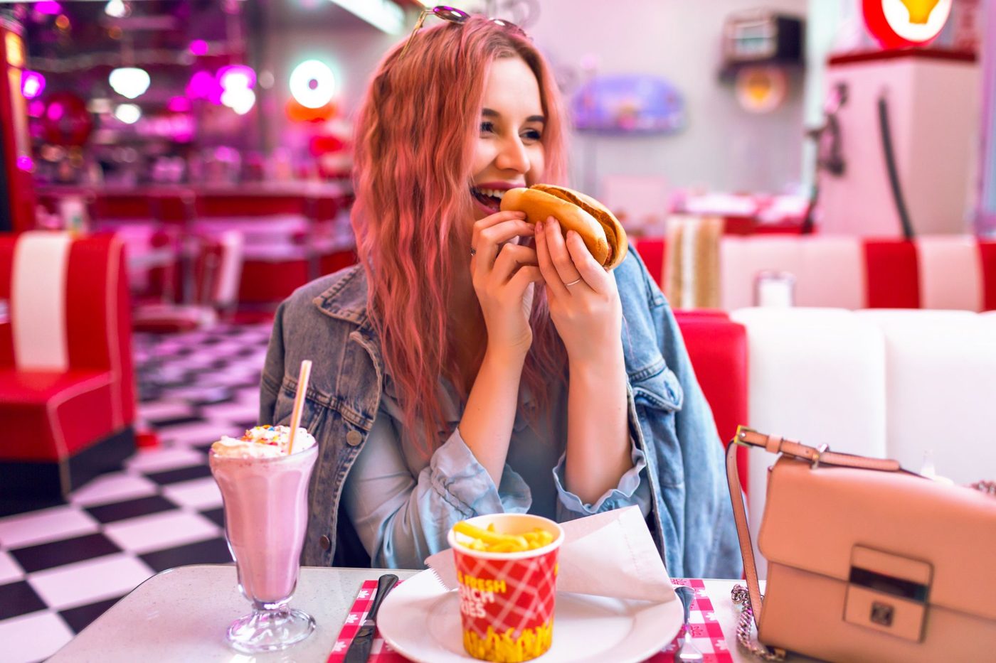 A woman eats a hot dog with a milkshake in a retro diner