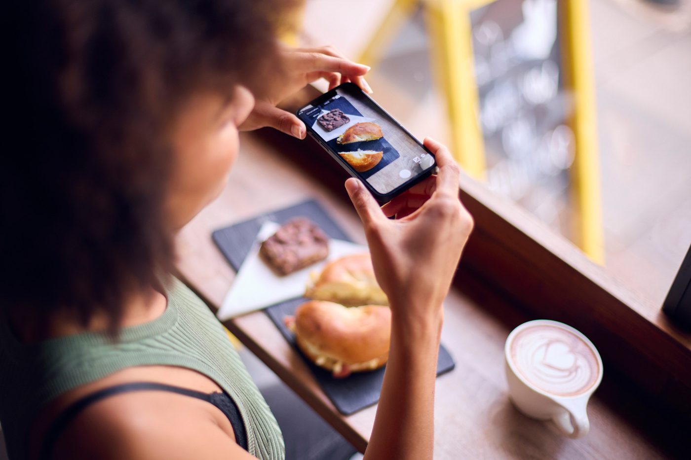 A customer photographs her bagel and brownie at a cafe window
