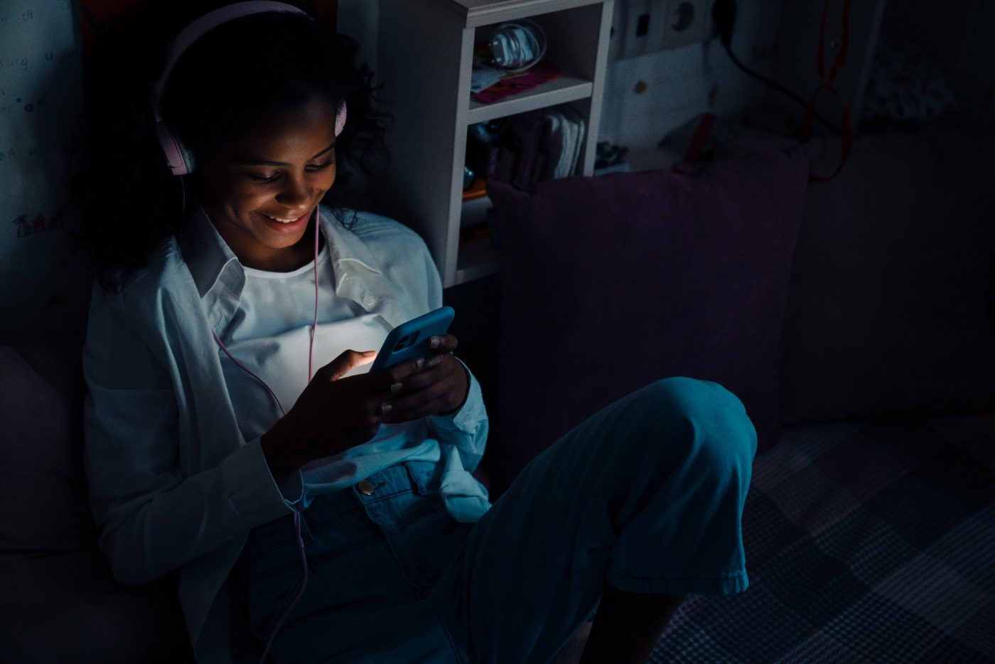 A woman in headphones smiles at her phone at night