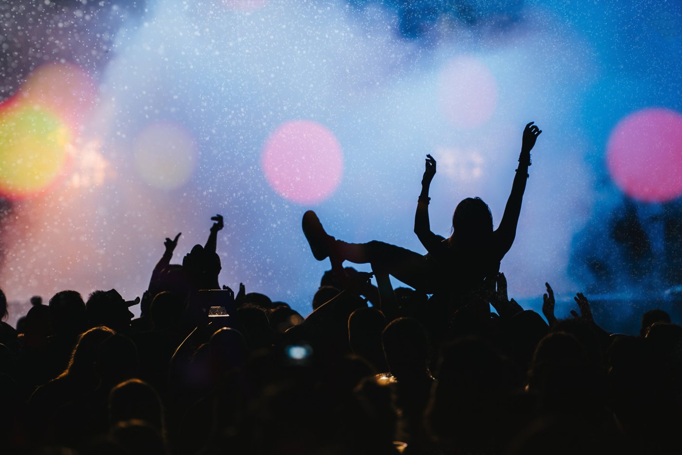 A festival crowd with a crowd-surfer under the stage lights
