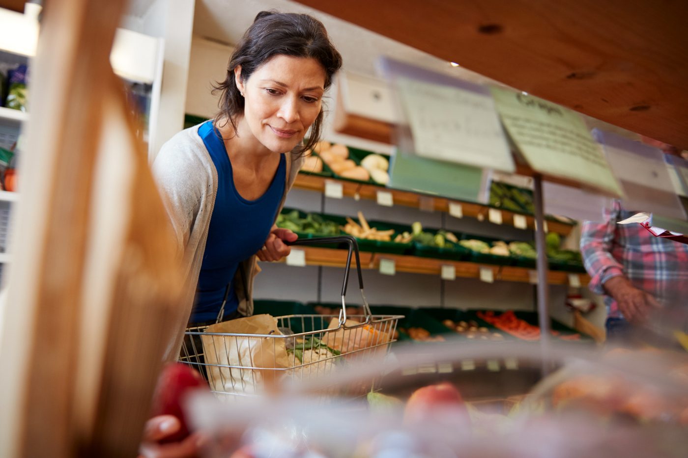 A shopper with a basket choosing fresh produce at the grocer