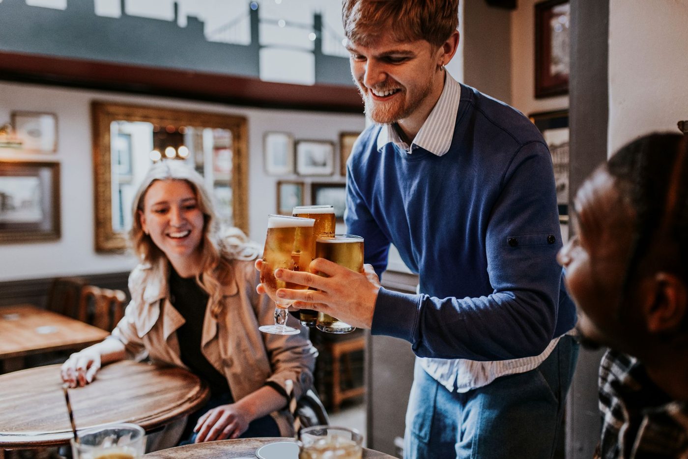 A smiling regular bringing a round of pints back to the table at the pub