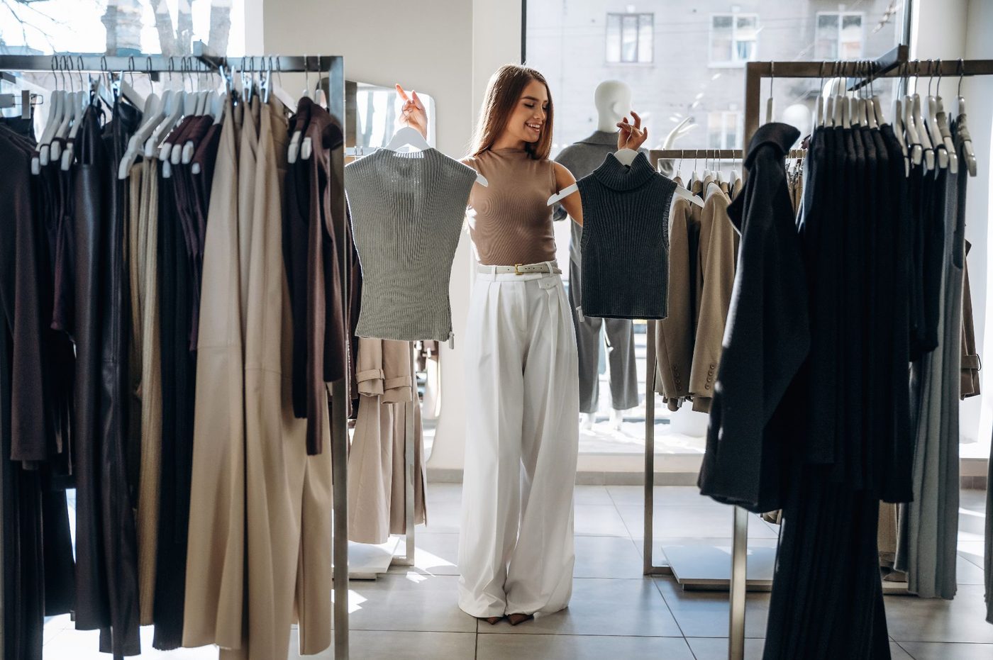 A woman holds up two knit tops in a clothing boutique