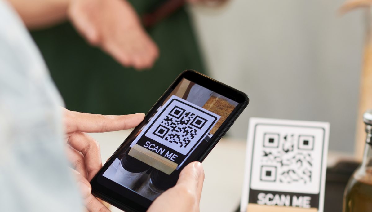 A customer scanning a “Scan me” QR code on their phone at a counter