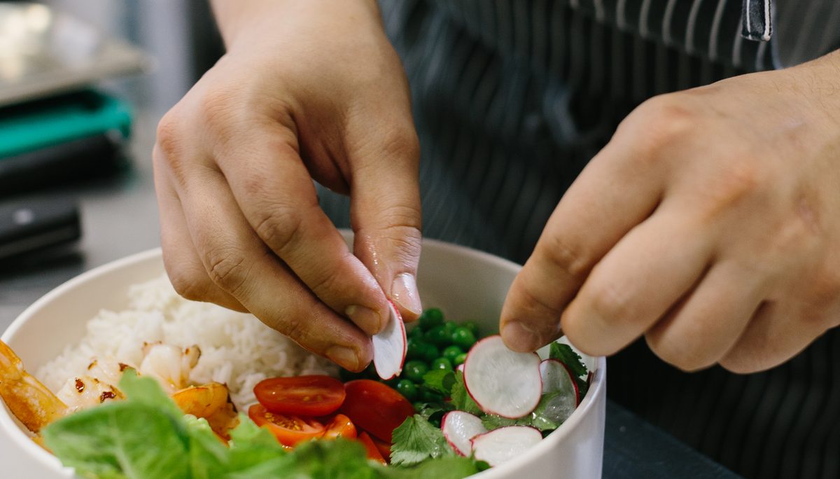 A chef adding sliced radish to a fresh rice bowl