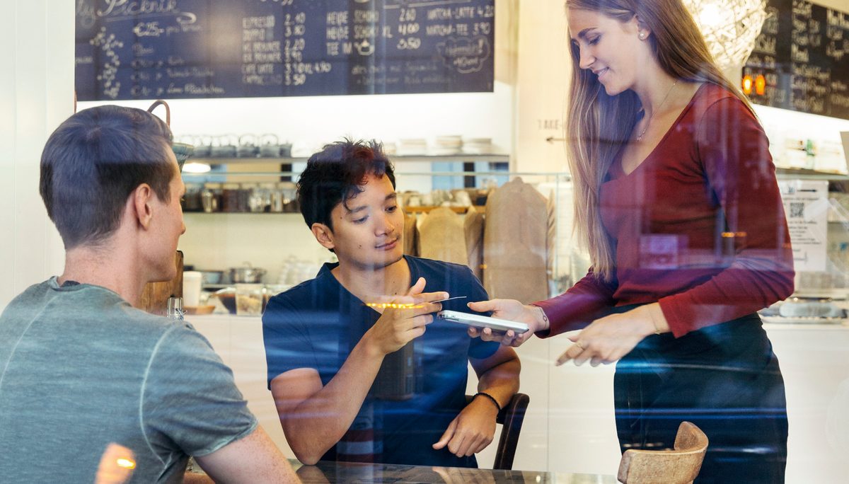 A café server showing two customers something on her phone at their table
