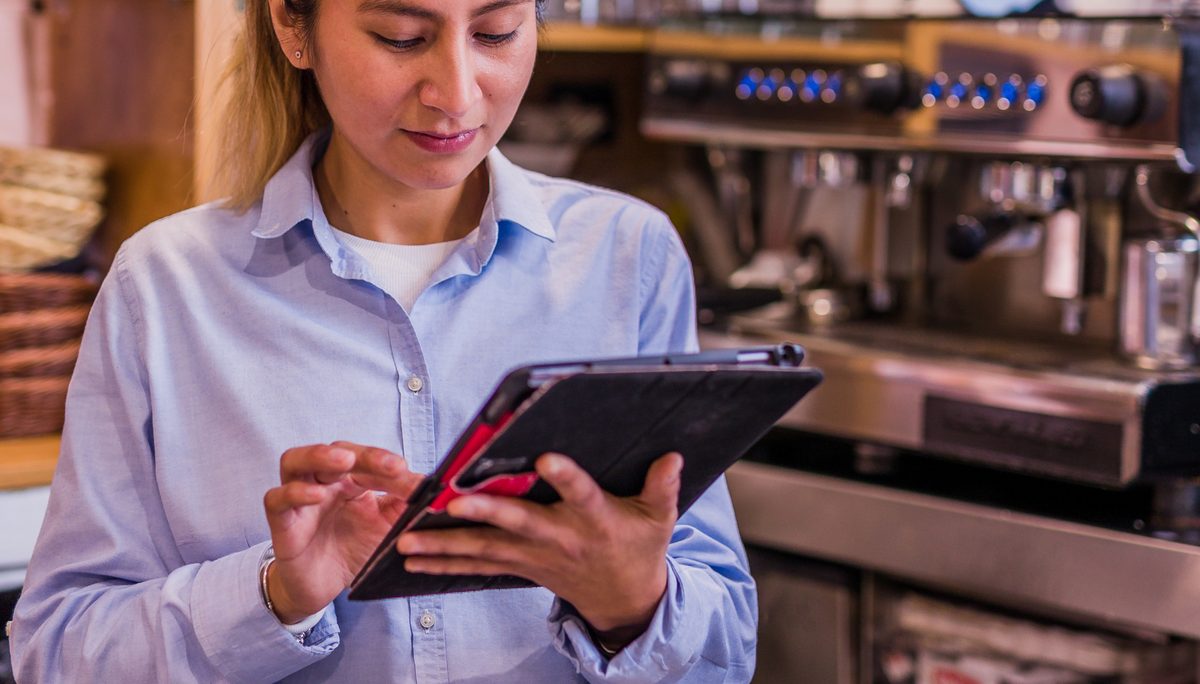 A café owner using a tablet beside the espresso machine