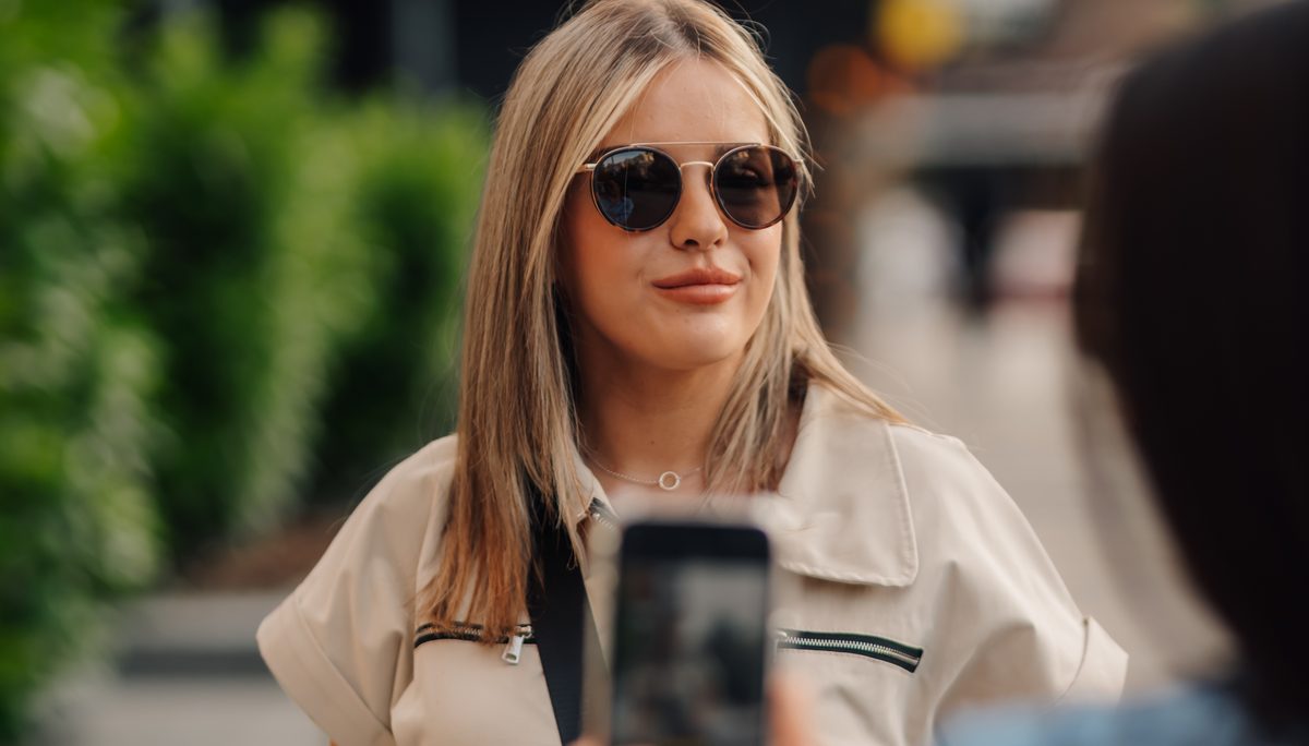 A woman in sunglasses being filmed on a phone outdoors