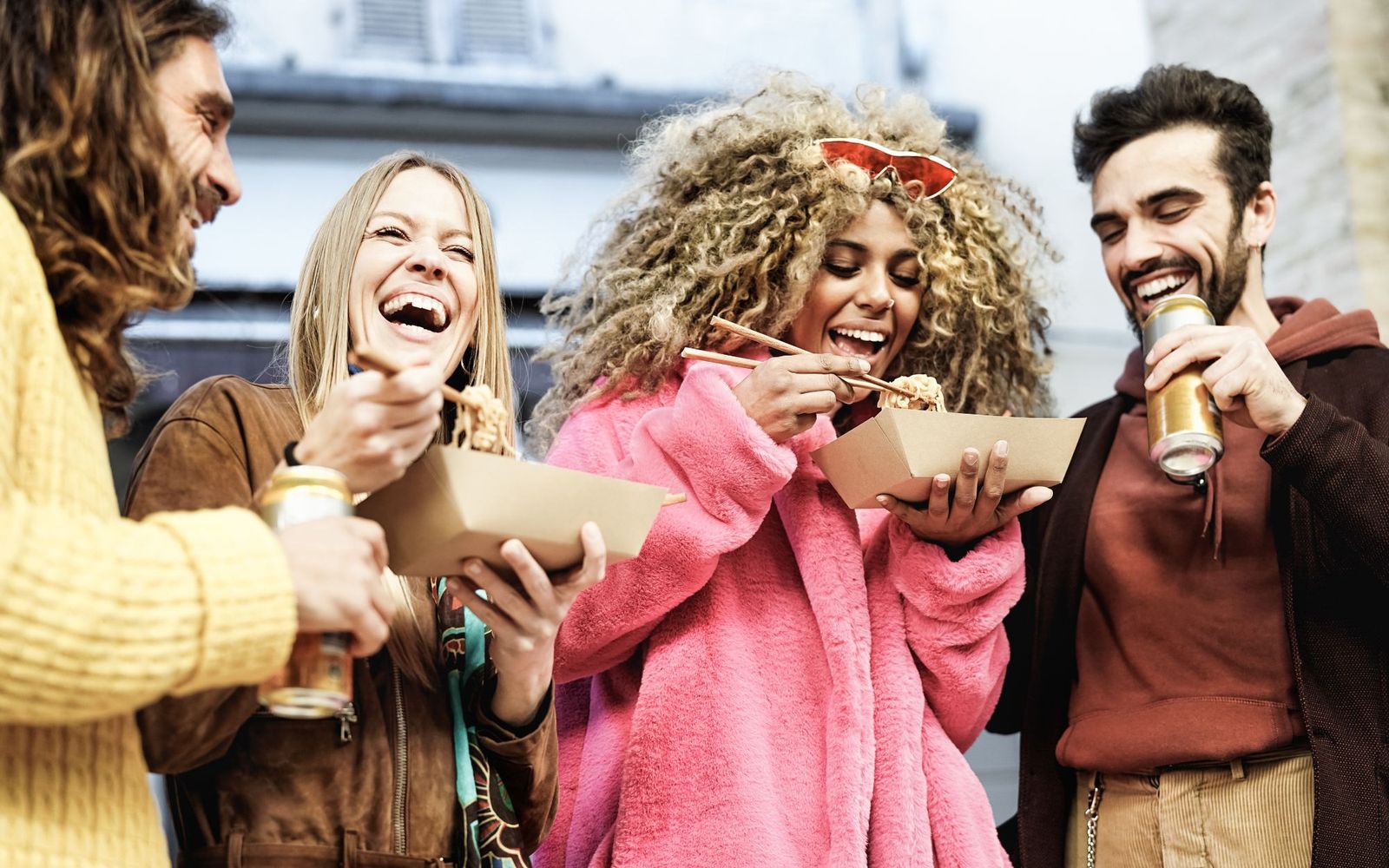 Friends laughing together over takeaway noodles and drinks