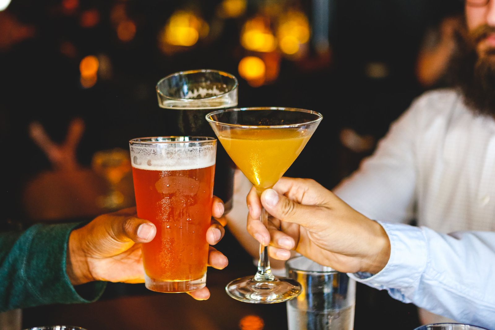 Friends raising a beer and a cocktail in a toast at the bar