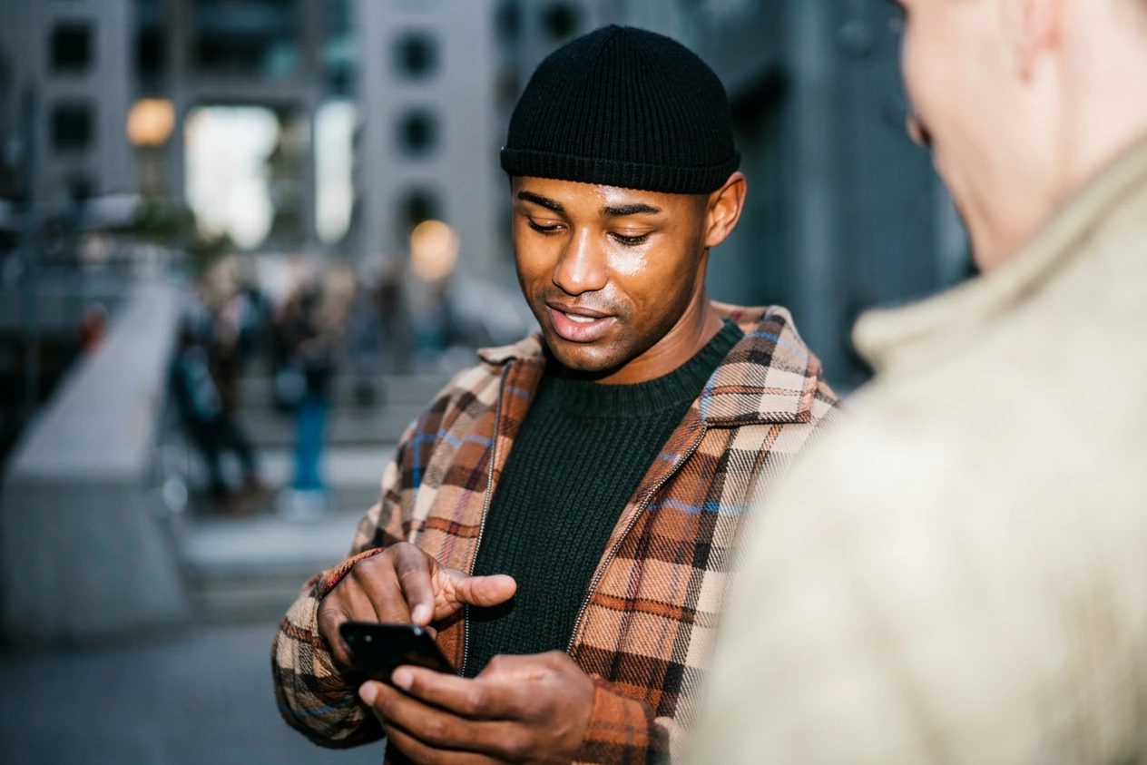 A young man smiling as he taps a notification on his phone in the street