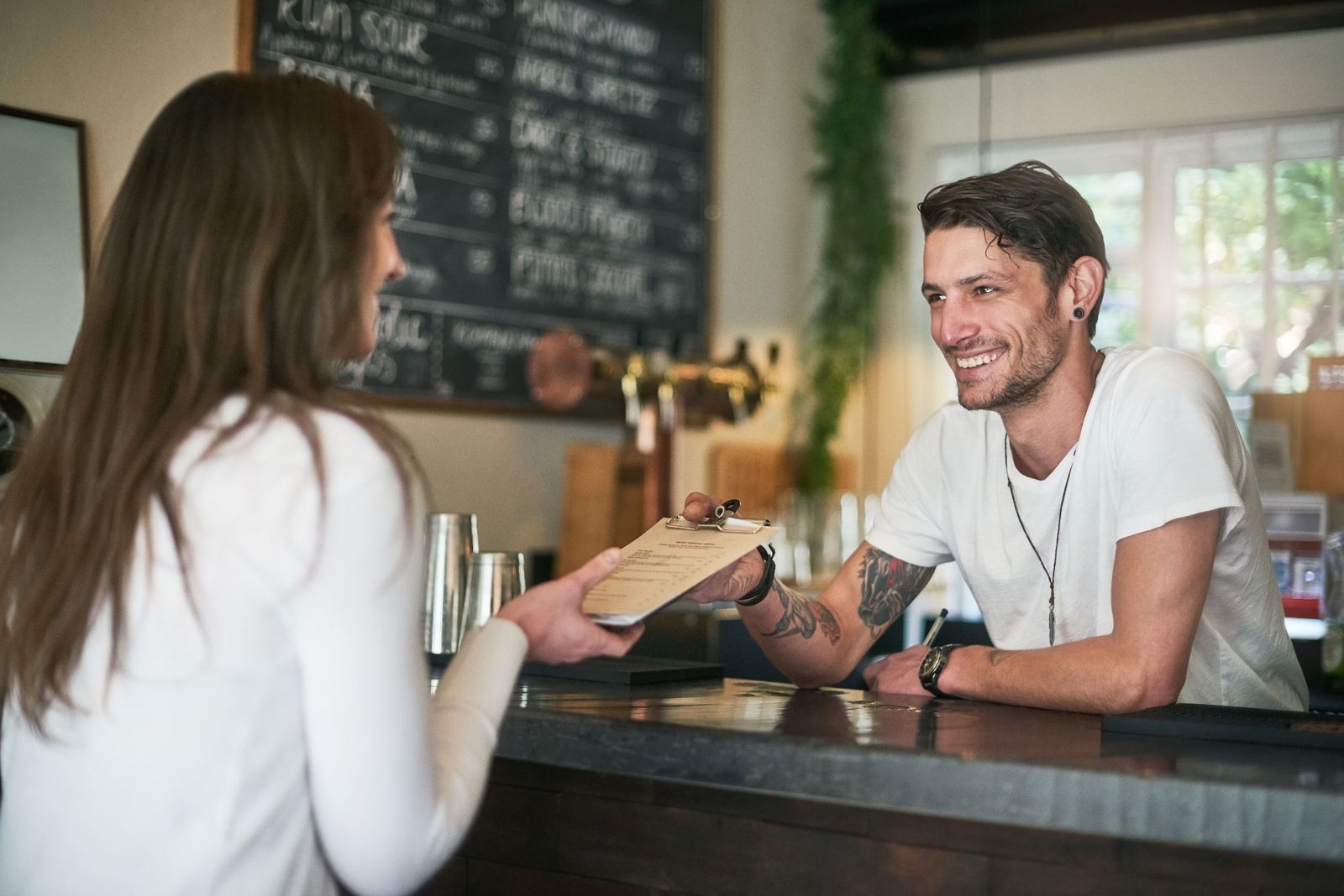 A bartender smiling as he hands a customer the menu across the bar